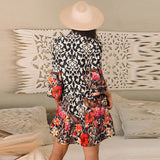 Woman wearing a boho-style long sleeve dress with ivory patterns and colorful floral print, standing in a cozy indoor setting.